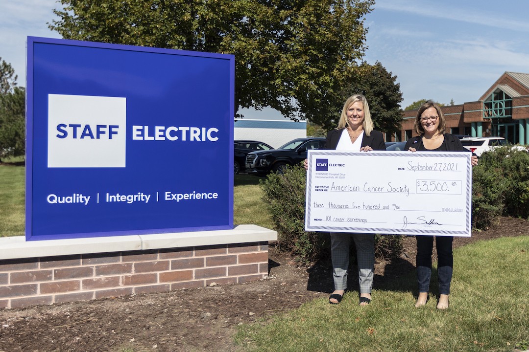 Two staff electric employees holding a check for the american cancer society.